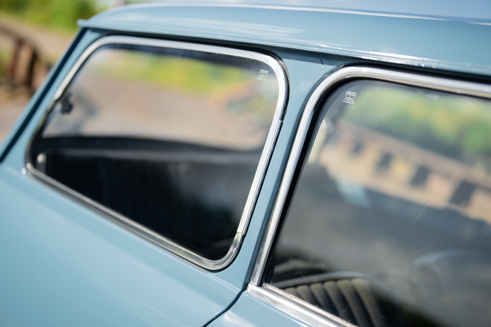 Close-up of a vintage car window, showcasing chrome trim and reflections of greenery.