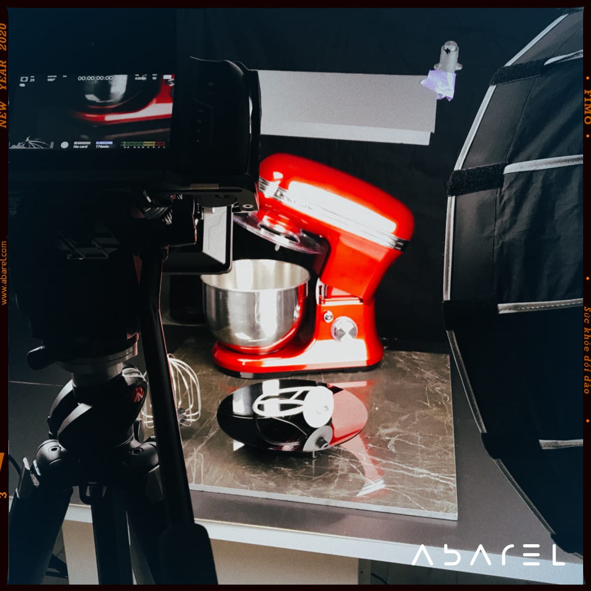 A rustic wooden table features a dark ceramic bowl filled with a fresh, colorful salad, including sliced mushrooms, chili, and vibrant mixed greens, surrounded by additional bowls of salad ingredients, lime wedges, and a golden spoon.