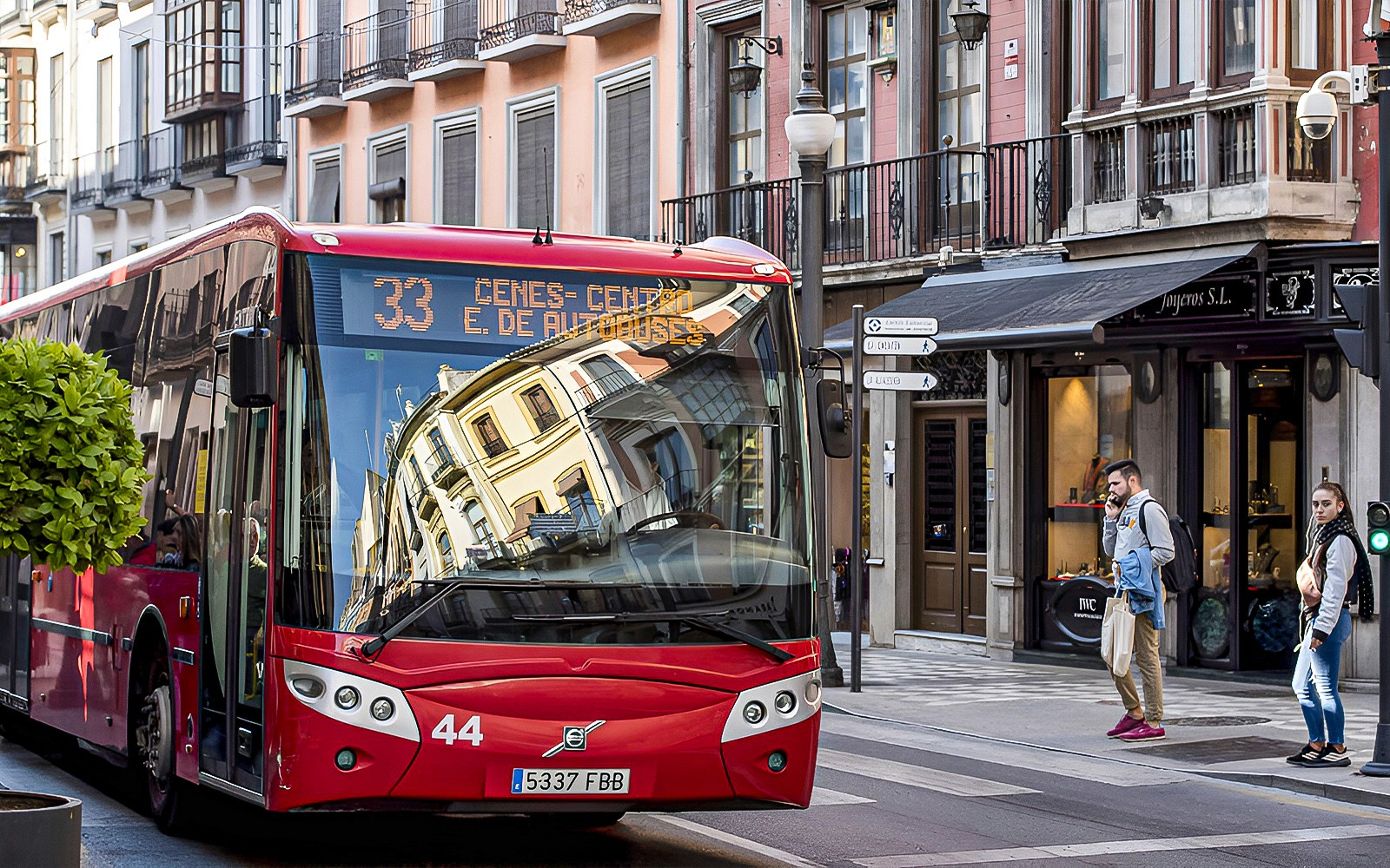Autobús rojo en una calle de Granada, España, cerca de tiendas y peatones.