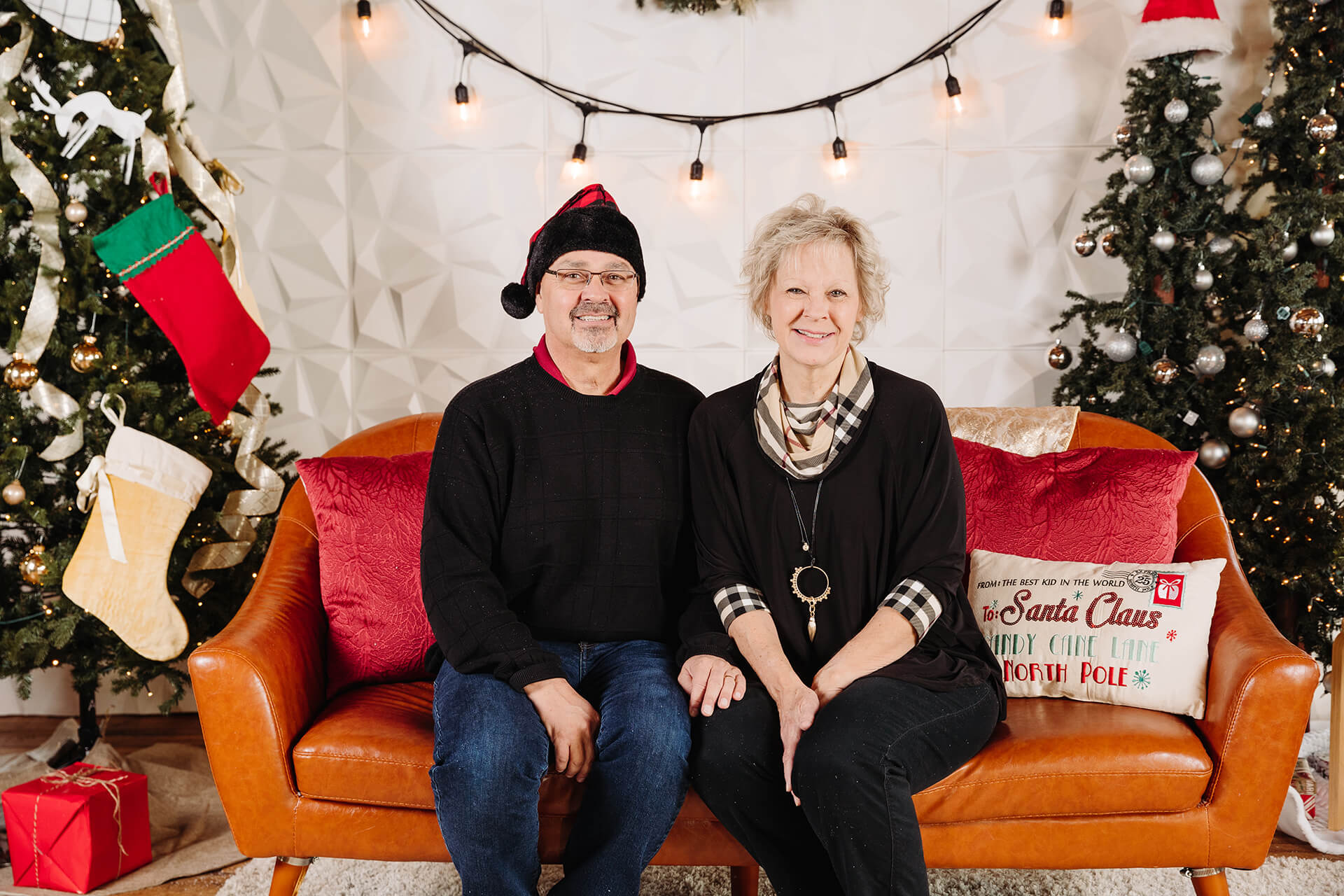 Photo of Mike and Nancy in Christmas outfits with decor surrounding them