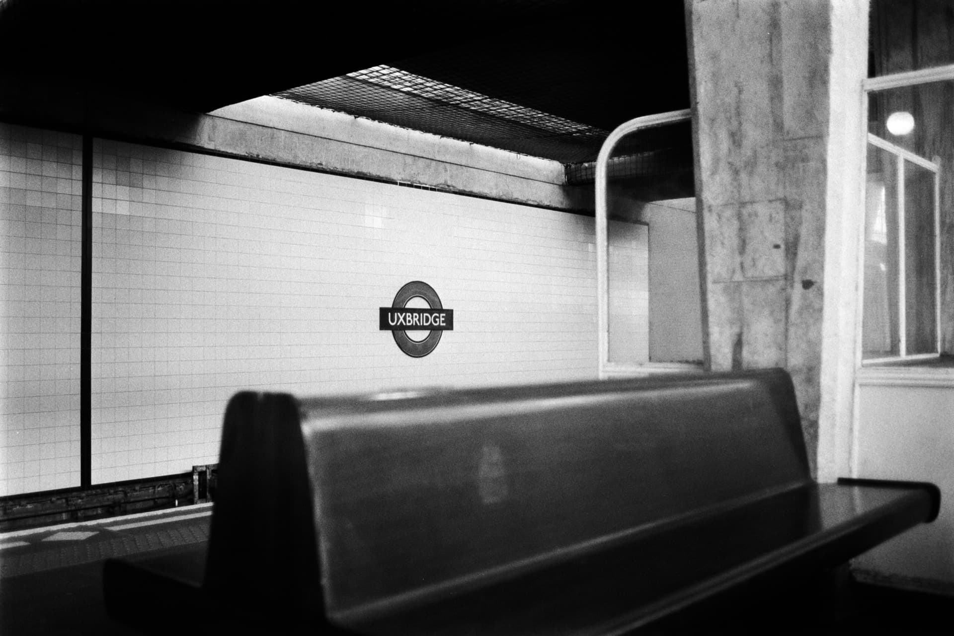 Uxbridge station roundel sign on white tiled wall with empty platform seating