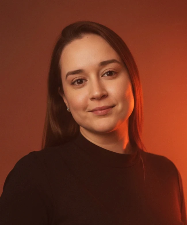 Portrait of a woman with straight long hair, in a dark t-shirt, set against a neutral backdrop.
