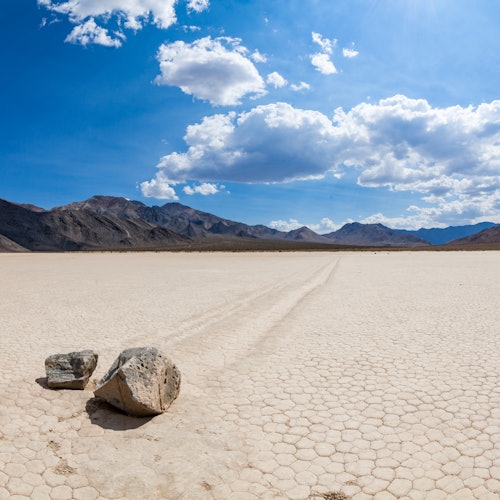 Two rocks on a dry, cracked ground with distant mountains under a partly cloudy sky.