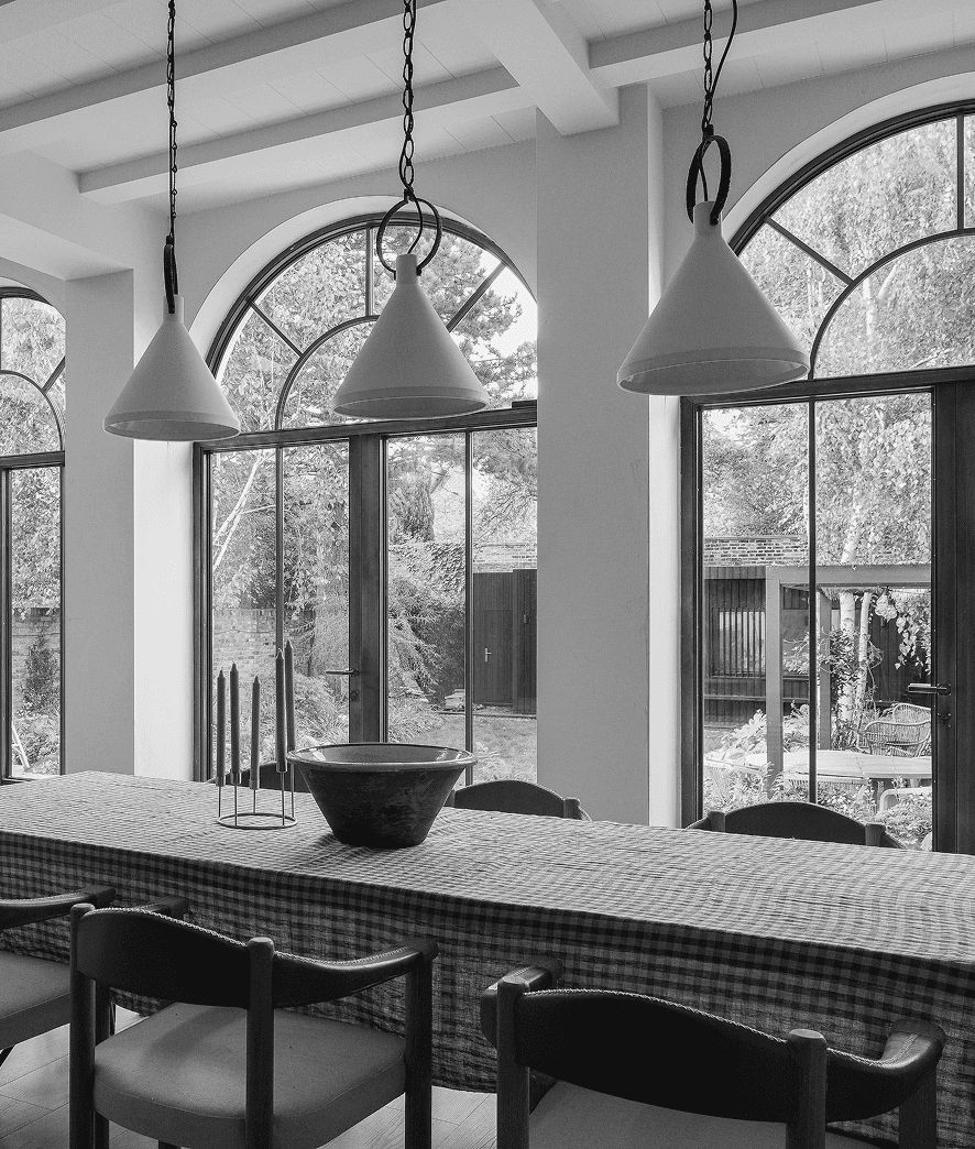 A modern kitchen with a long counter, bar stools, and large windows letting in natural light. Black and white image.