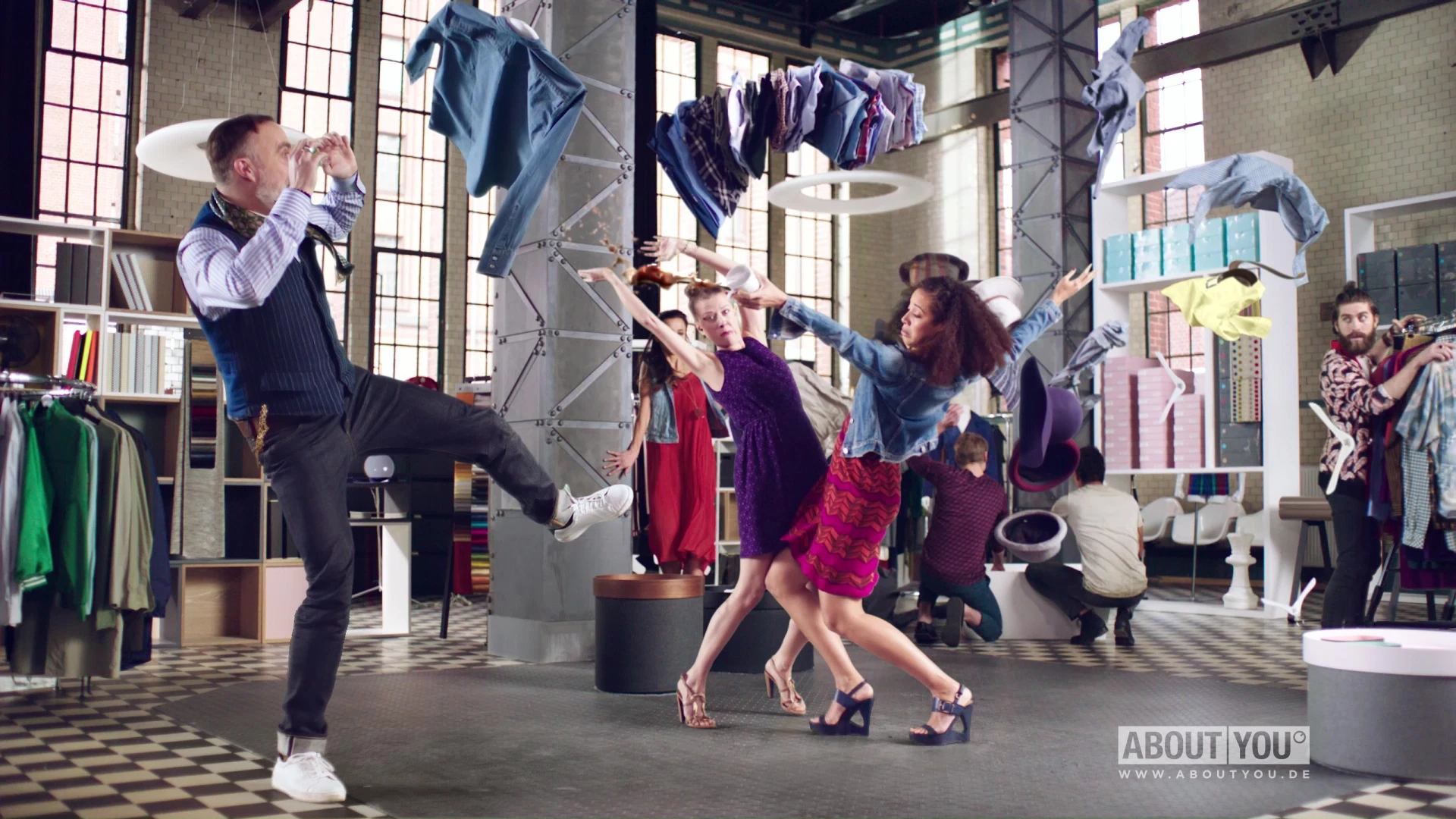 Two fashionable women carrying stacks of clothing crash into each other as a man jumps back in surprise.