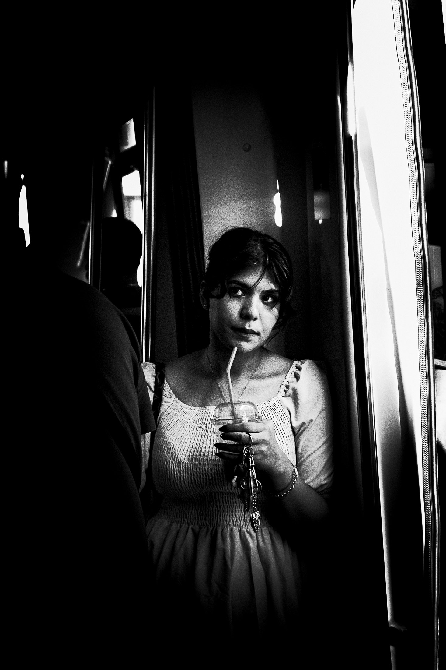 Woman standing inside a train holding a drink and keys, intimate black and white street photography.