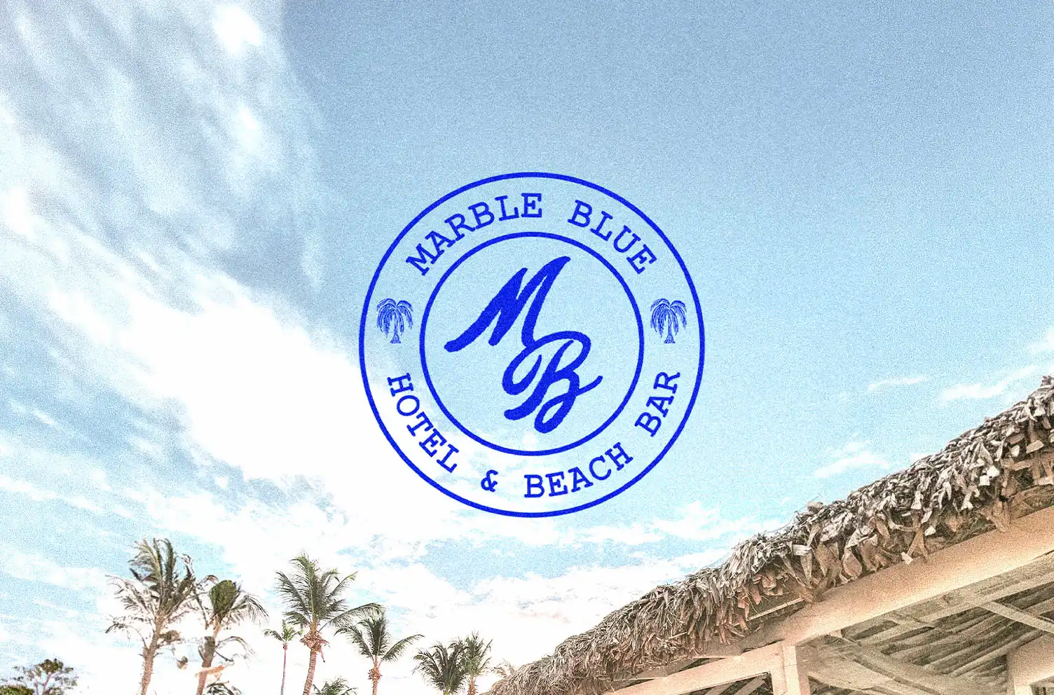 Logo circulaire Marble Blue Hotel & Beach Bar en bleu cobalt sur fond de ciel et toiture en paille, avec monogramme MB en script au centre.