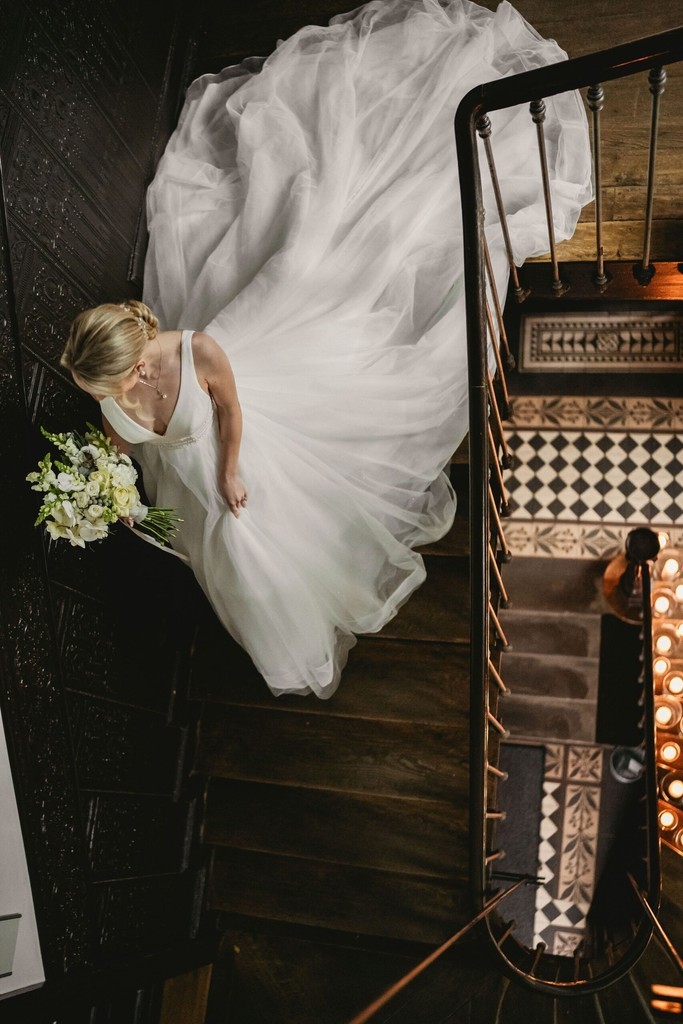Braut in weißem Kleid mit Strauß auf Treppe von oben gesehen