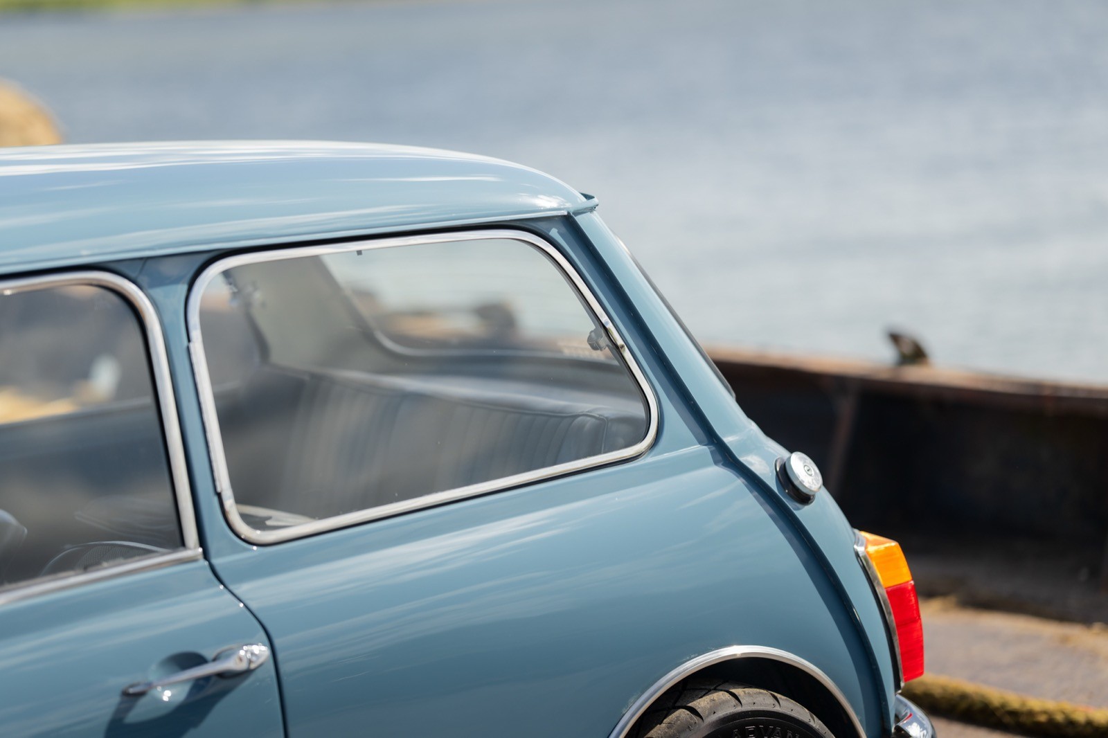 Classic blue car parked near a body of water, with a partially visible shoreline in the background.