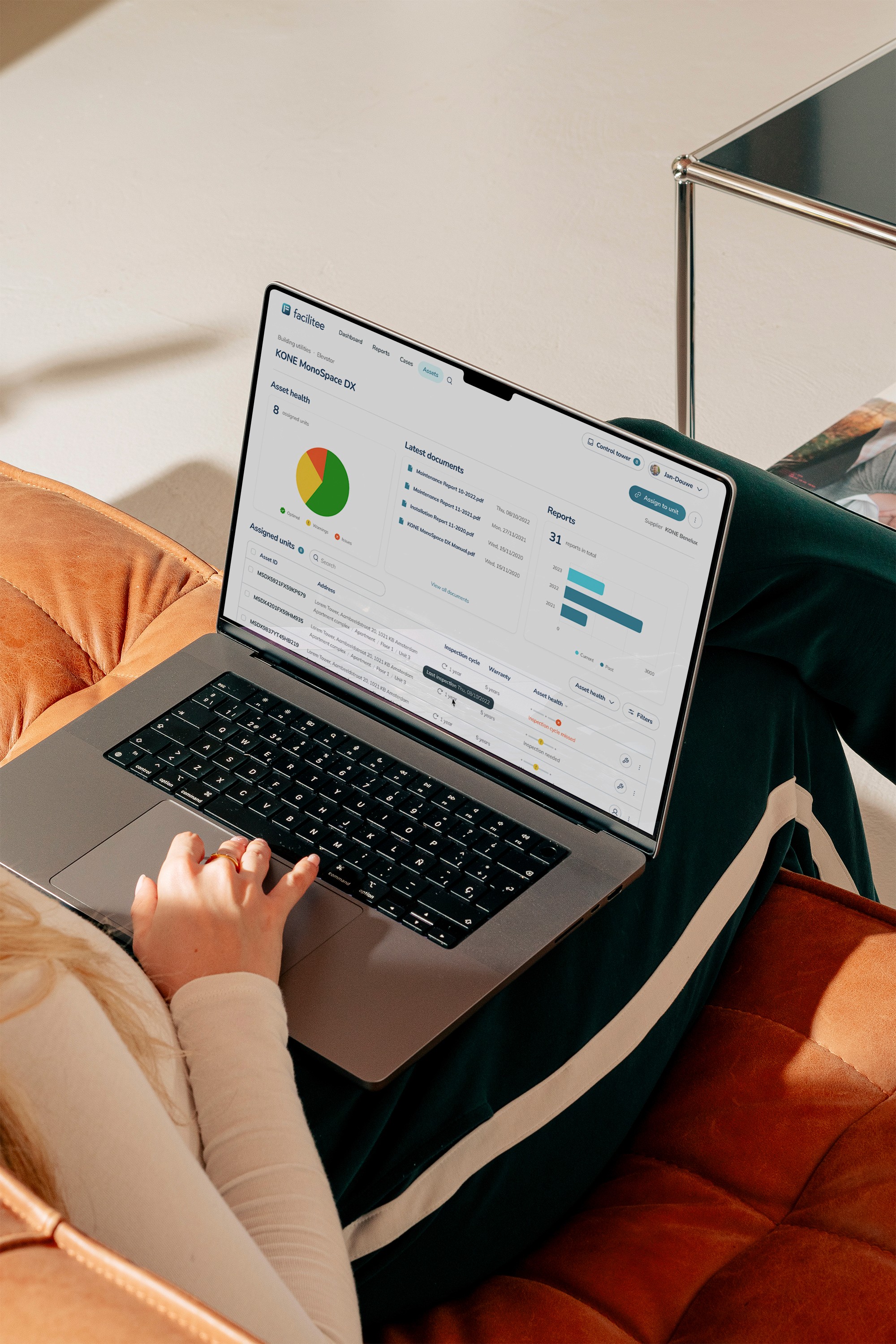 A woman sitting on a sofa with a laptop on her lap, showing a dashboard on the screen.