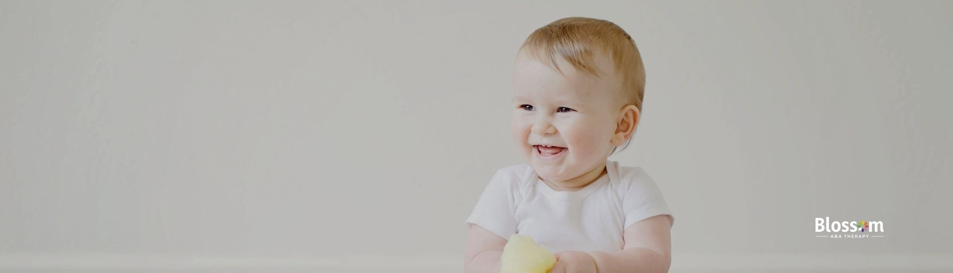 A baby sits and smile, while holding a yellow fabric.