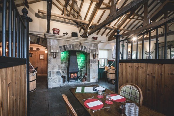 Rustic dining room in converted stable featuring exposed wooden beams, original horse stalls and cozy stone fireplace