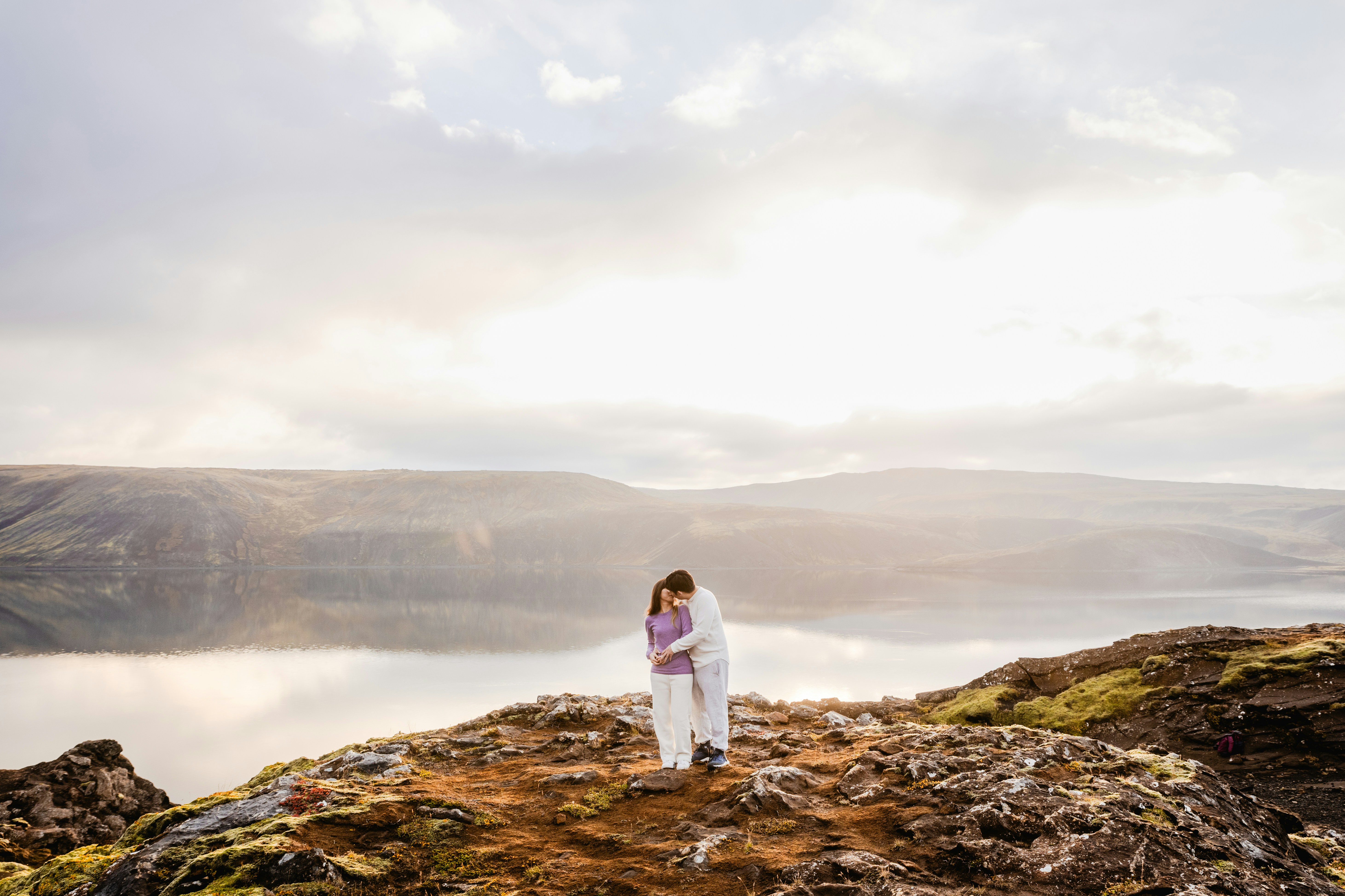 A couple standing on a large volcanic rock overlooking Kleifarvatn Lake in Iceland.