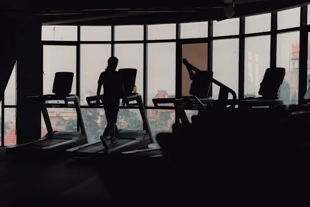 Person walking on a treadmill in a gym with large windows and city light