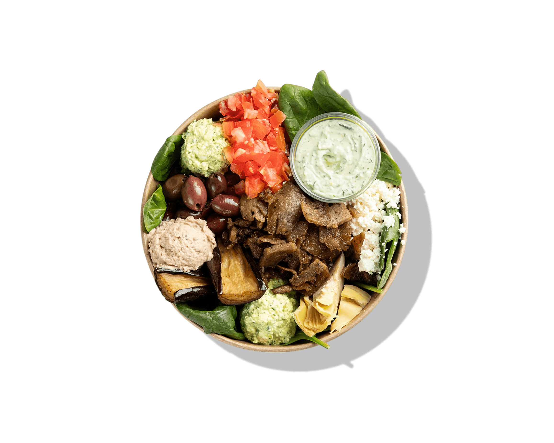 top down shot of bowl with greens, various vegetables, gyro, scoops of hummus, & small container of sauce