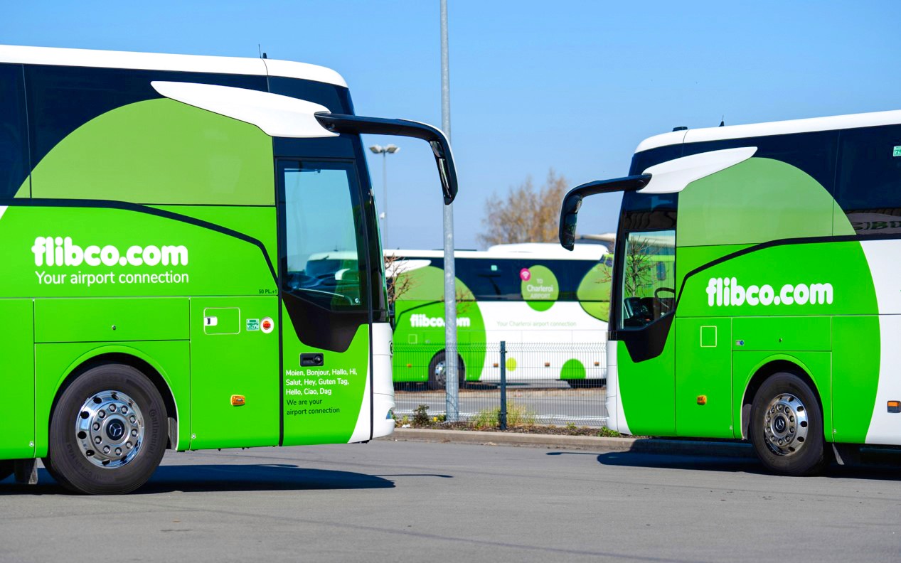 Grüne Flughafenshuttlebusse, die auf einem Parkplatz stehen, mit sichtbarem flibco.com-Branding.