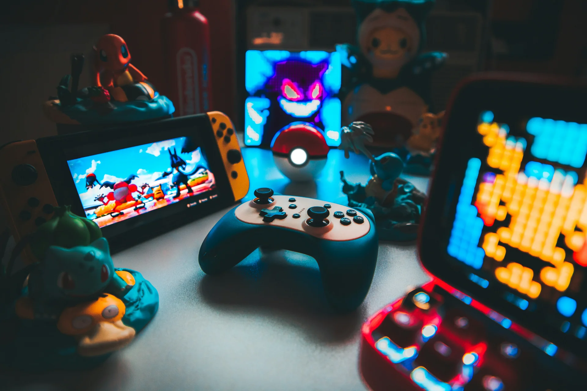 Nintendo Switch, controller, and retro arcade screens surrounded by Pokémon figures on a dark desk