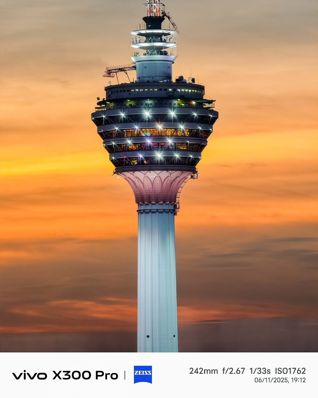 A close-up view of a tall observation tower against a vibrant sunset sky, displaying colorful lighting on its structure, highlighting the details of the tower's design.
