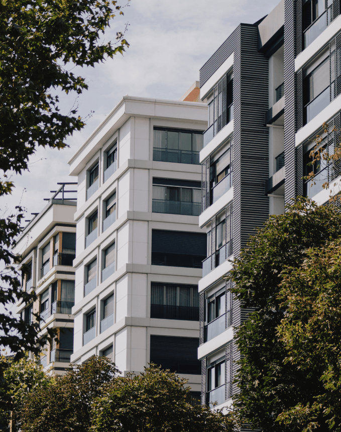 A serene outdoor seating area with two chairs, surrounded by lush greenery and a glassed-in structure.