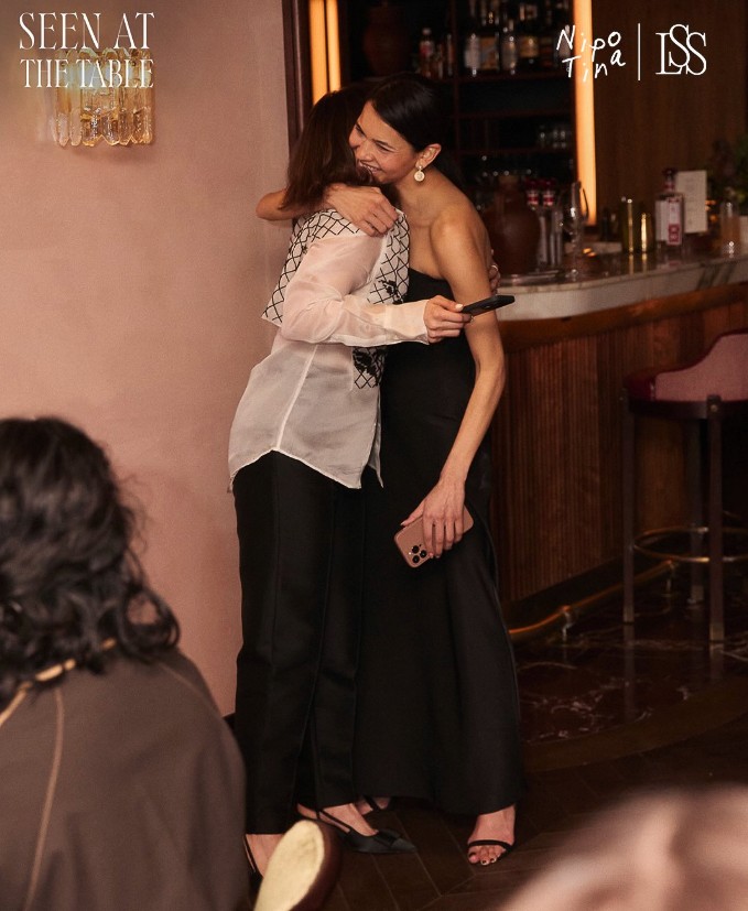 A diverse group of six people are sitting around a table in a well-lit conference room. They are engaged in a discussion, with laptops and papers on the table.