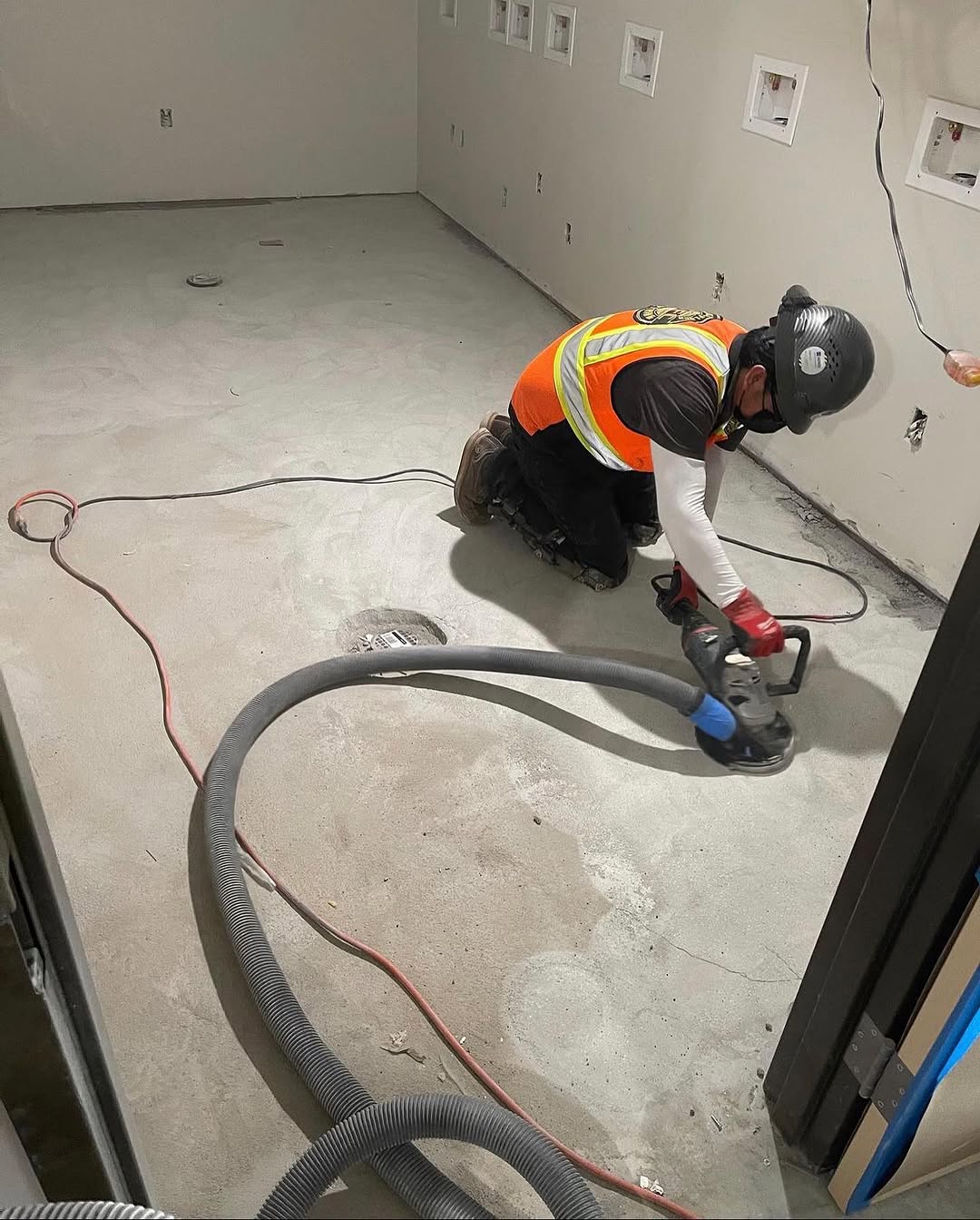 Installer grinding a concrete slab with a dust-extraction vacuum before underlayment
