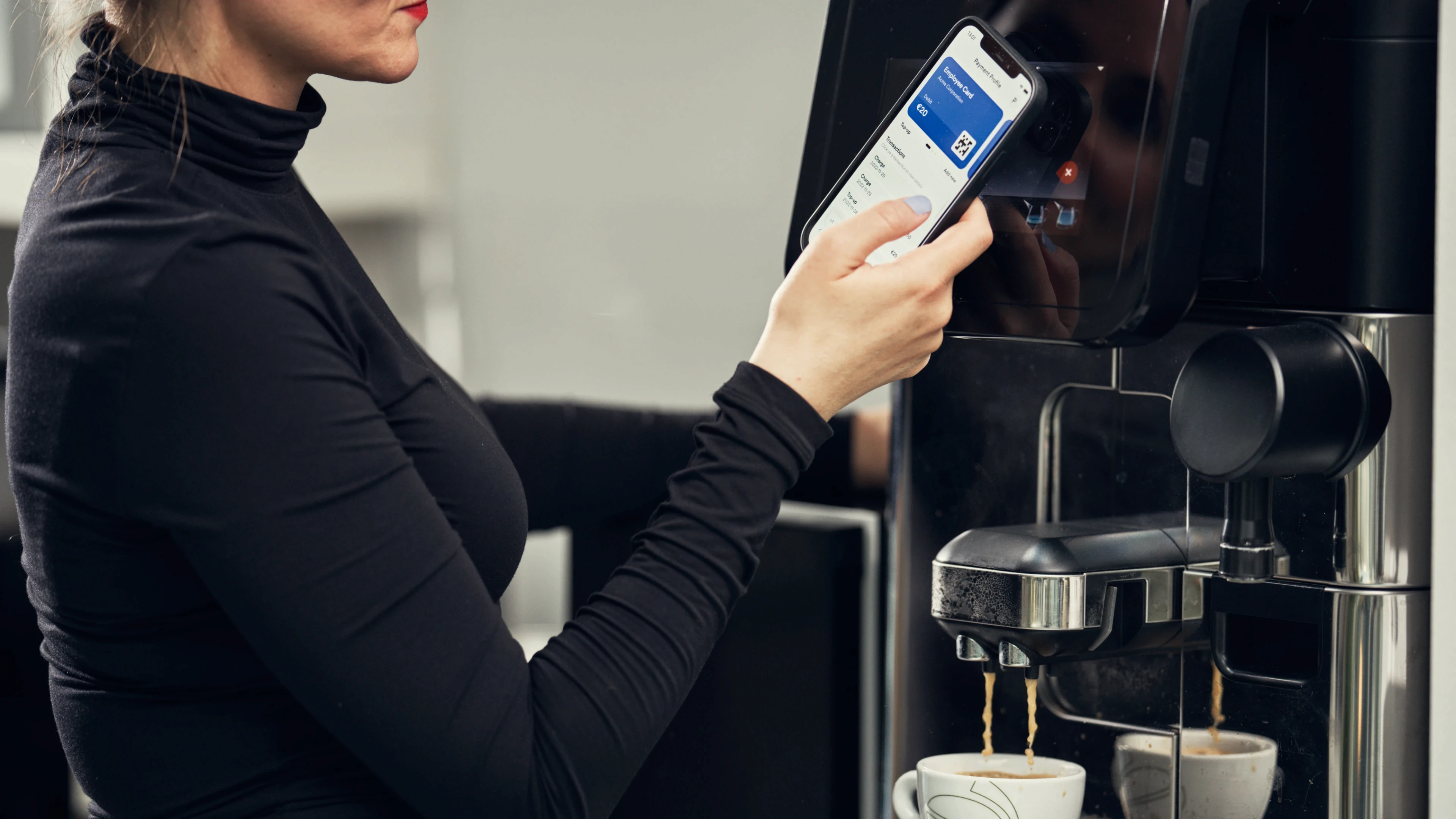 A woman purchasing a coffee at a coffee machine using her Pej Guest App