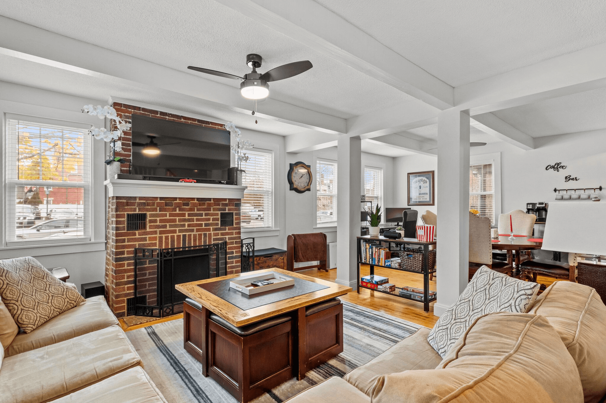 Bright and cozy Airbnb living room with white columns, large windows, a mounted TV over a brick fireplace, and comfortable beige seating in one of the top 1% of Airbnb listings for guest satisfaction.
