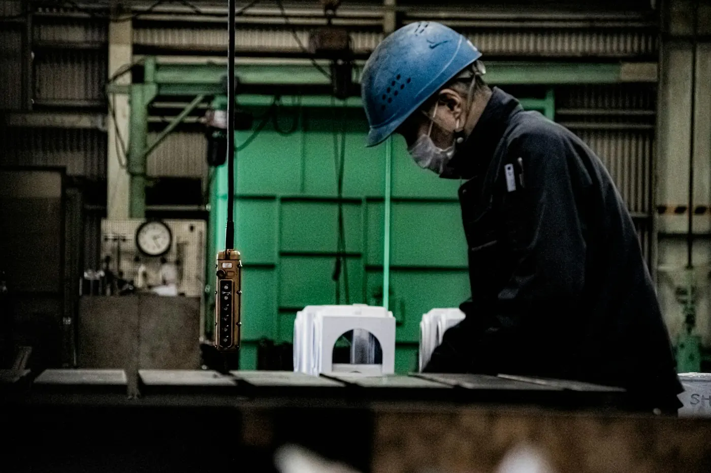 Factory worker in a hard hat and face mask working at a machine