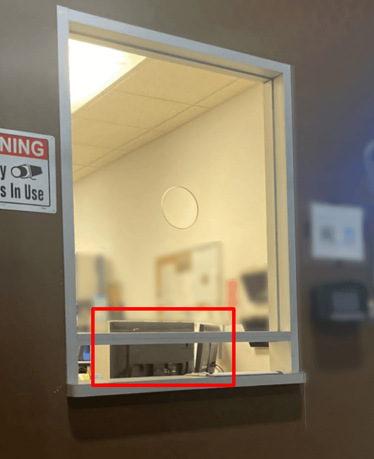 An image of a front desk area with a glass barricade. A red box outlines the computer monitors, which are easily accessible to visitors.