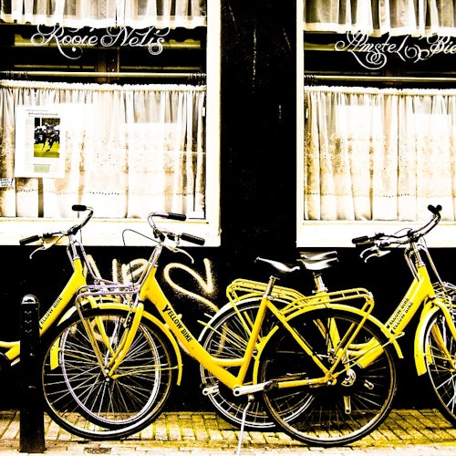 三辆黄色自行车停在一个带有窗帘的黑色店面前，墙上可见涂鸦。