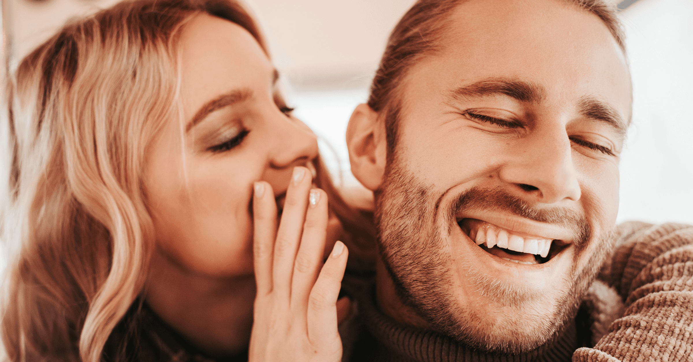 En kvinne hvisker i en manns øre, og mannen smiler bredt.