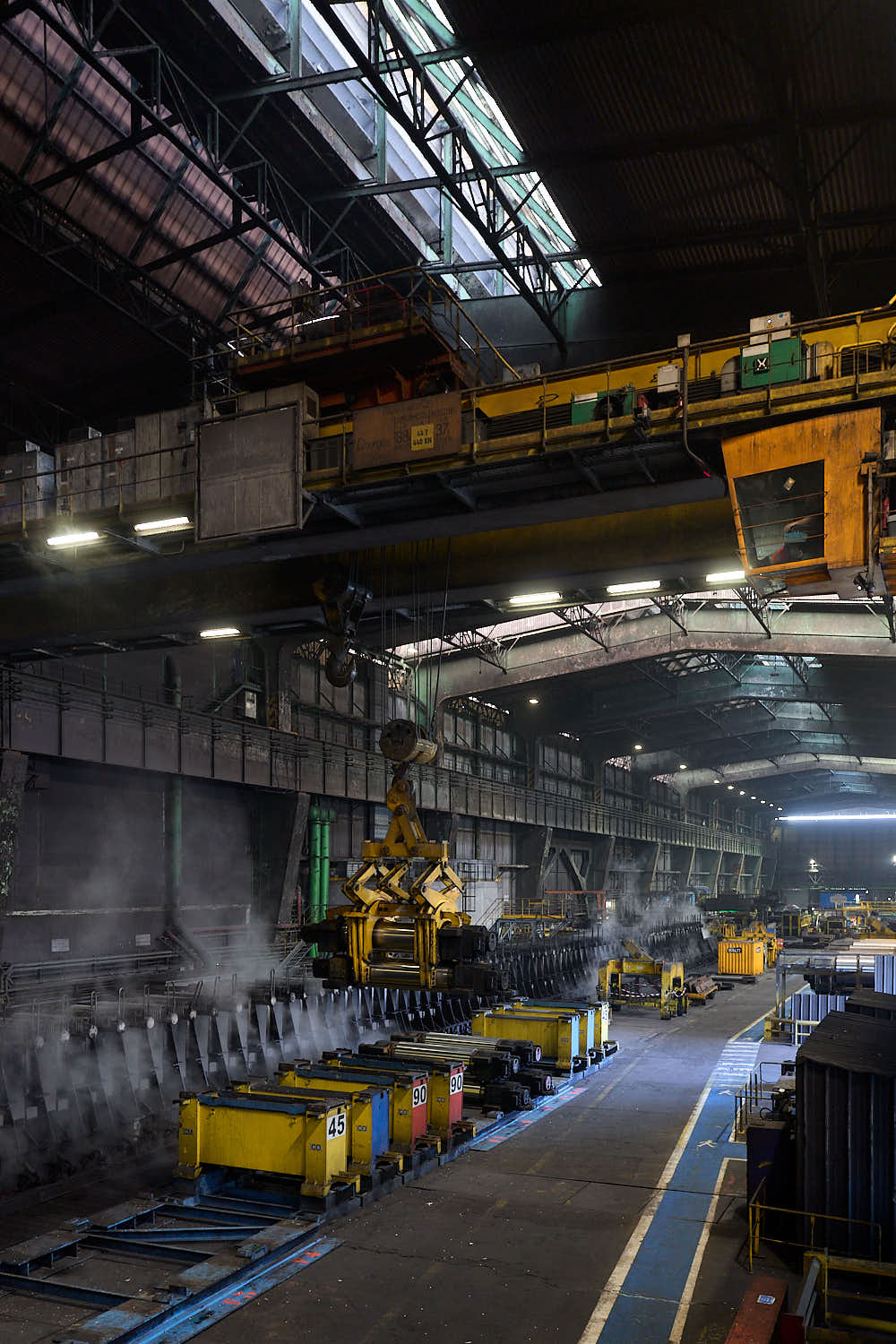 Hangar industriel ArcelorMittal avec une grue qui porte une pièce de remplacement d'un rouleau de laminoire.