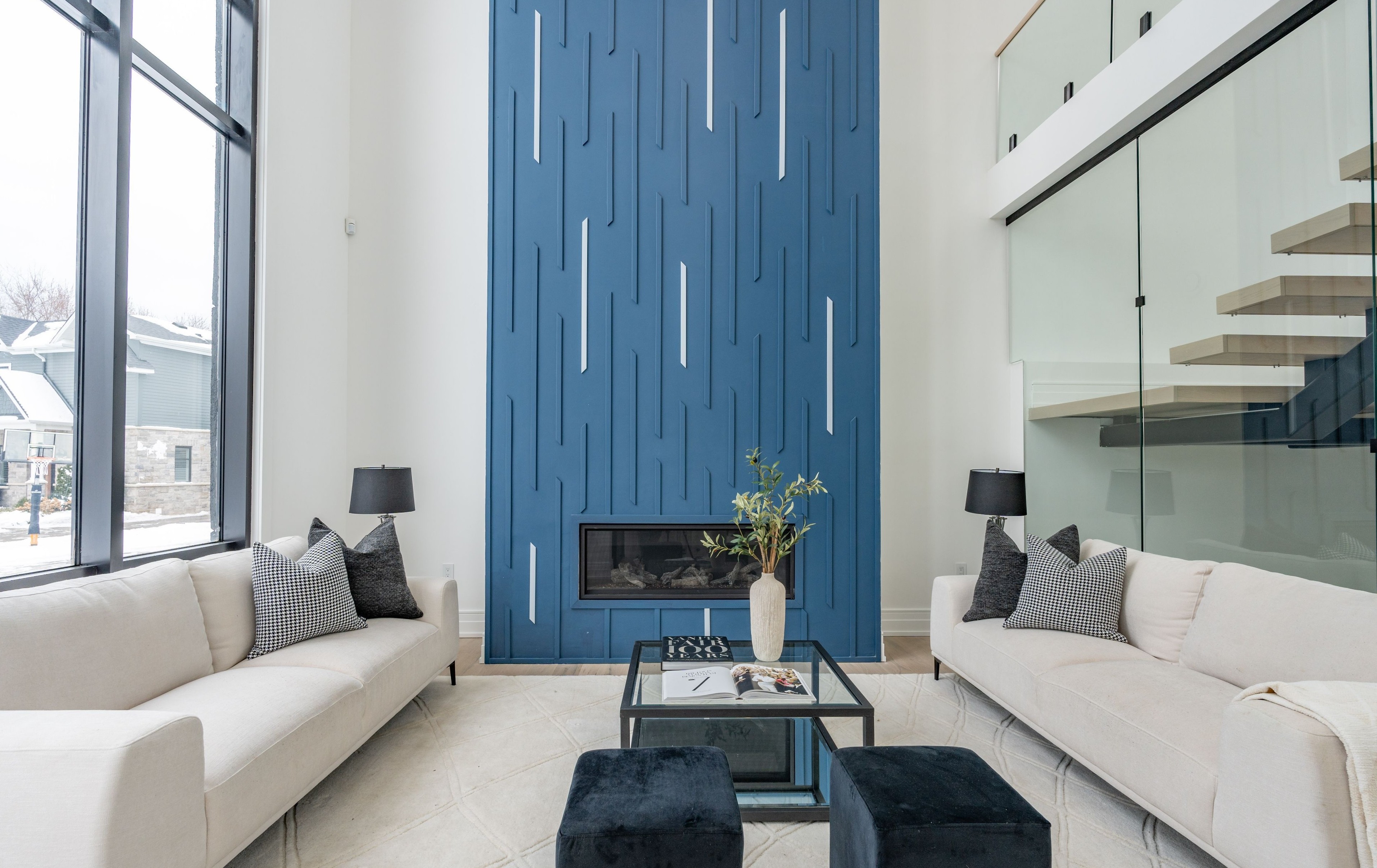 A modern hallway features vibrant teal and orange geometric and leaf patterns, with glossy tiled floors, a large rectangular light fixture, and a small shelf holding a potted plant, all leading to a large, frosted window at the end.