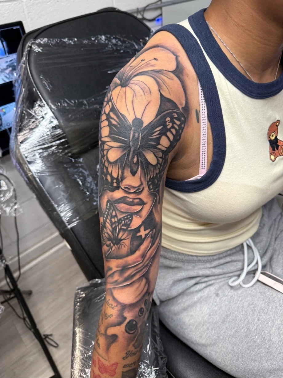 Black-and-gray butterfly and portrait tattoo on an upper arm.