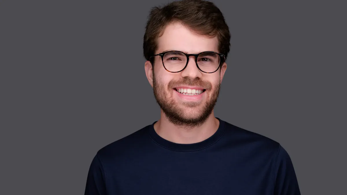 Brex-CEO Pedro Franceschi mit Brille und Bart in dunklem Shirt vor grauem Hintergrund. Die Stimmung ist fröhlich.