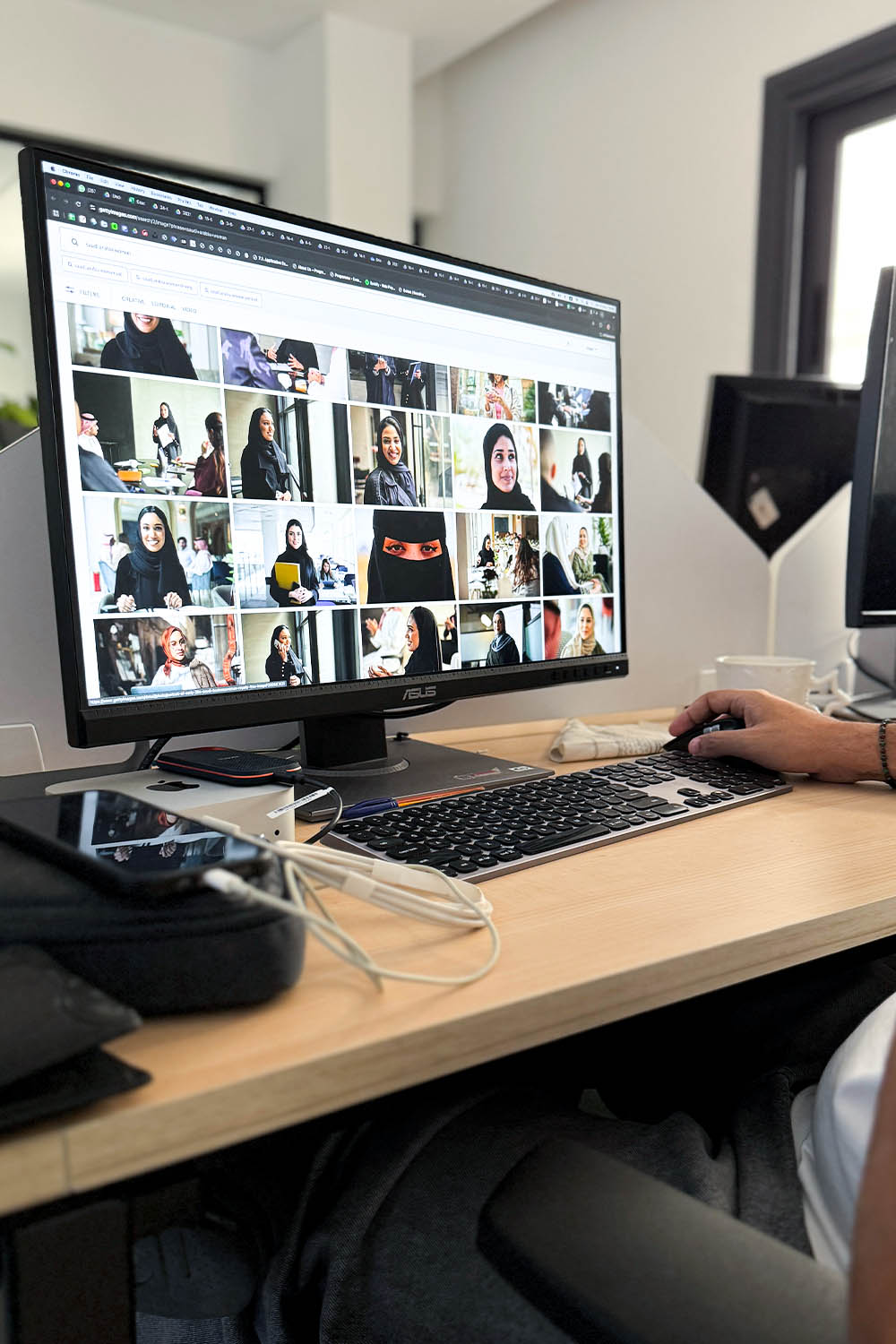 A person using a computer with multiple images displayed on the screen, sitting at a wooden desk.