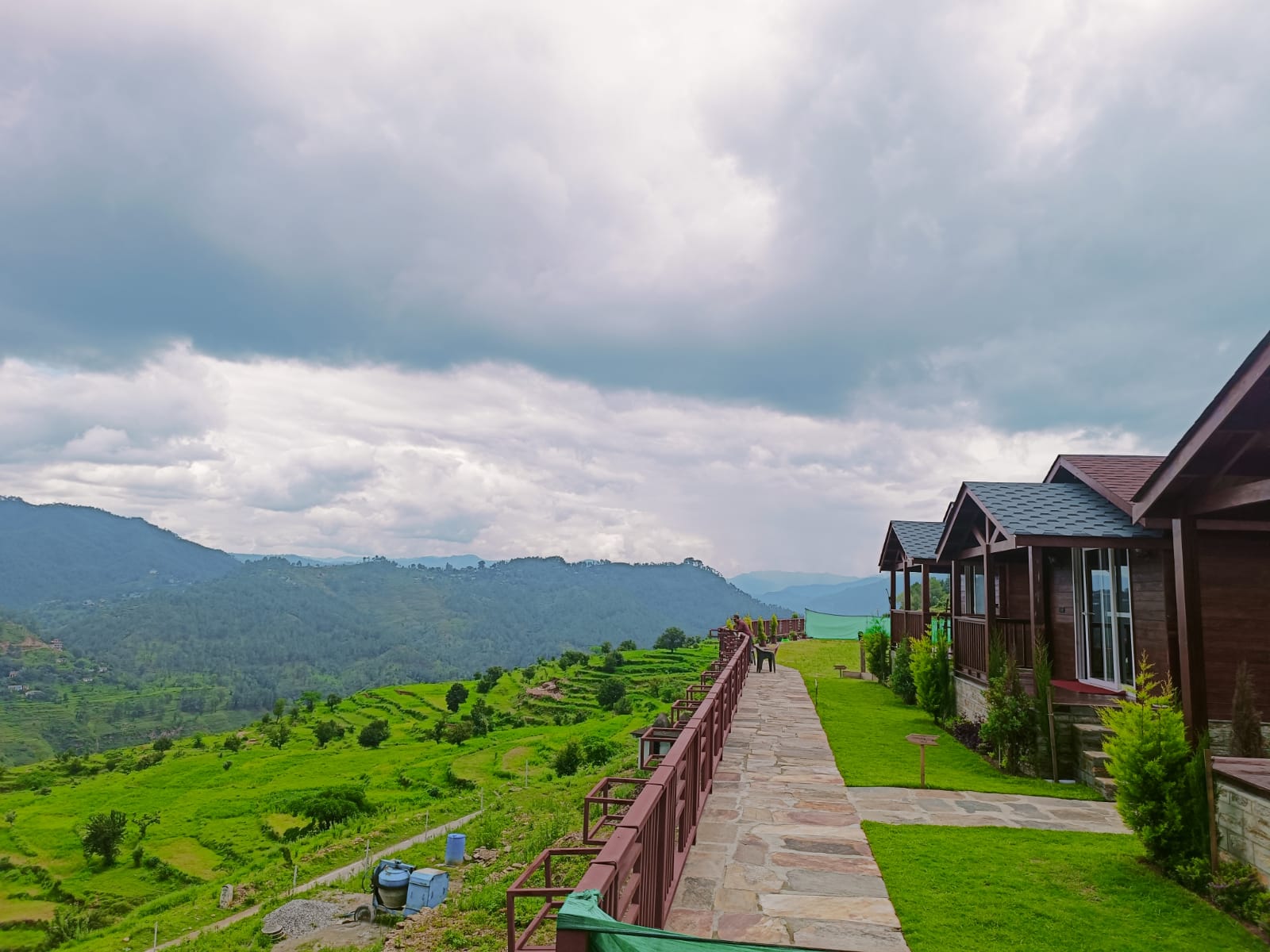 <img src="swiss-chalet-text.png" alt="A scenic view of a pathway lined with greenery, leading to distant hills under a cloudy sky." />