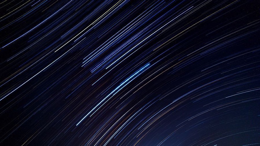 Long-exposure photograph of star trails creating curved blue and white light streaks across the night sky.