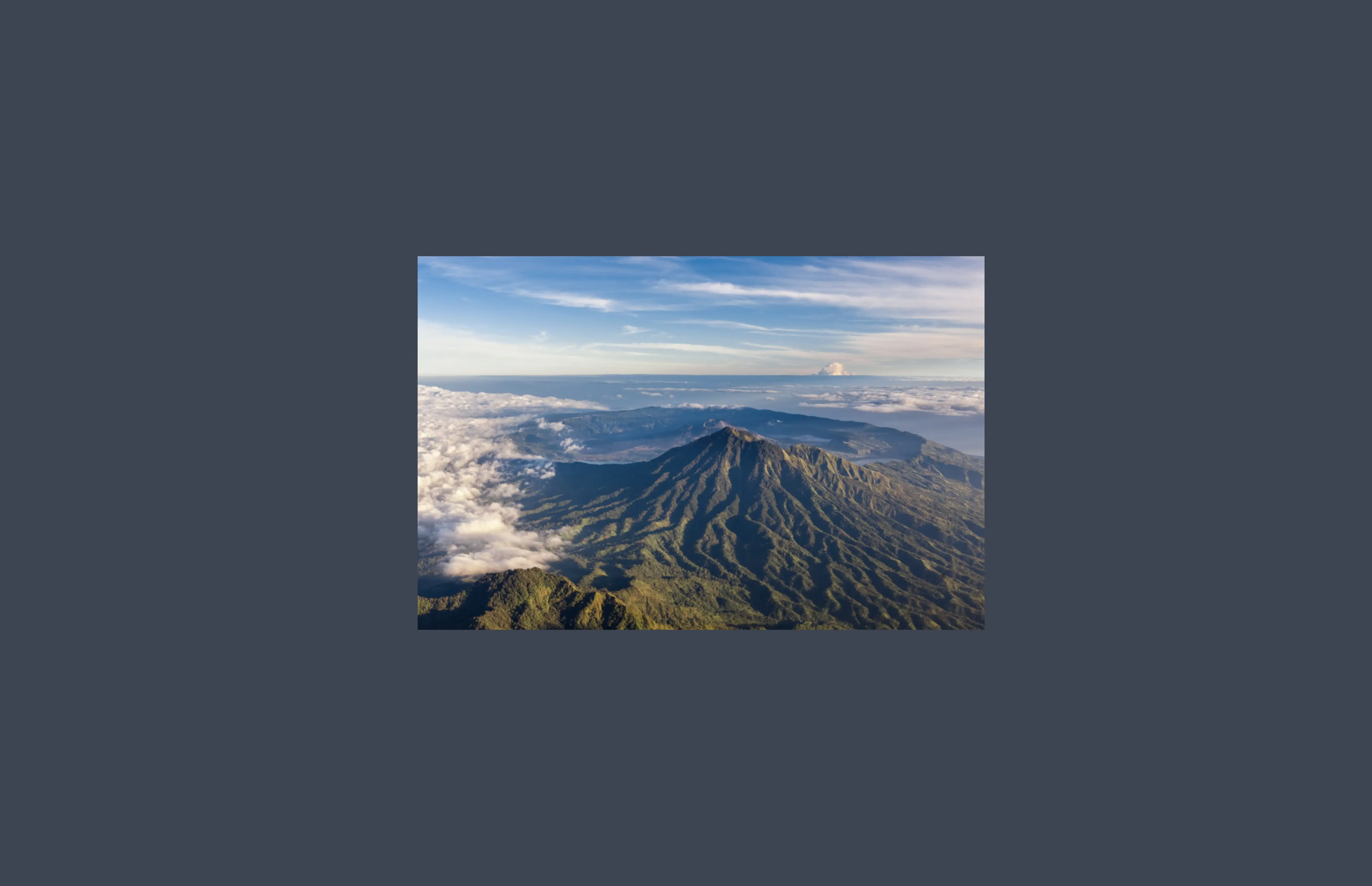 Aerial view of a Balinese volcano rising above the cloud line, showing the island's interior highlands.