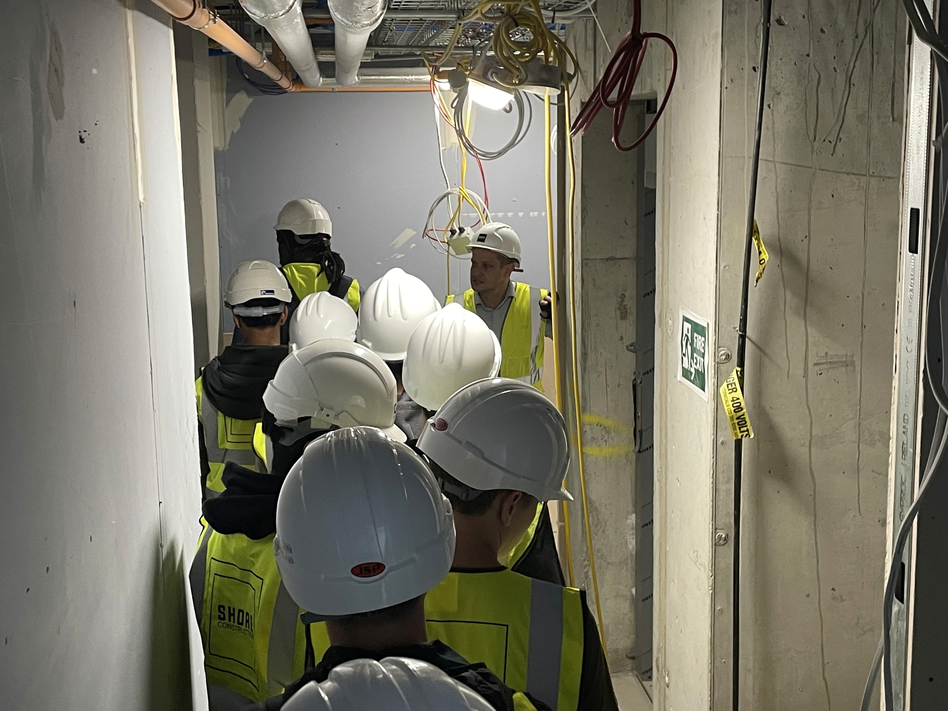 Construction engineers and workers conducting a site inspection inside an unfinished commercial building to review construction progress, electrical installations, and safety compliance.