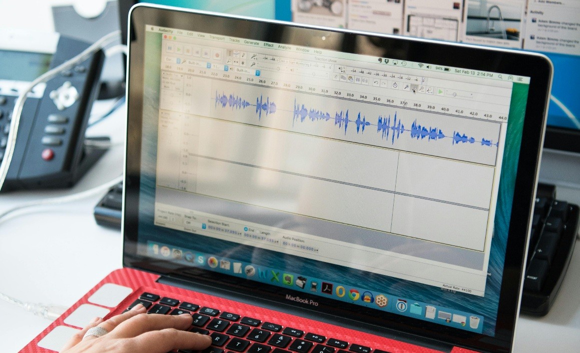 A laptop screen showing a podcast editing software interface, with waveforms of recorded audio and a person's hand operating the keyboard