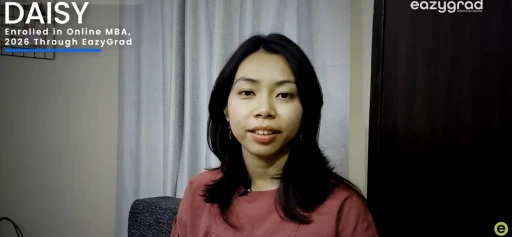 A woman wearing a pink shirt sits in a room with a curtain backdrop, looking directly at the camera, with text overlay mentioning enrollment in an online MBA program through EazyGrad.