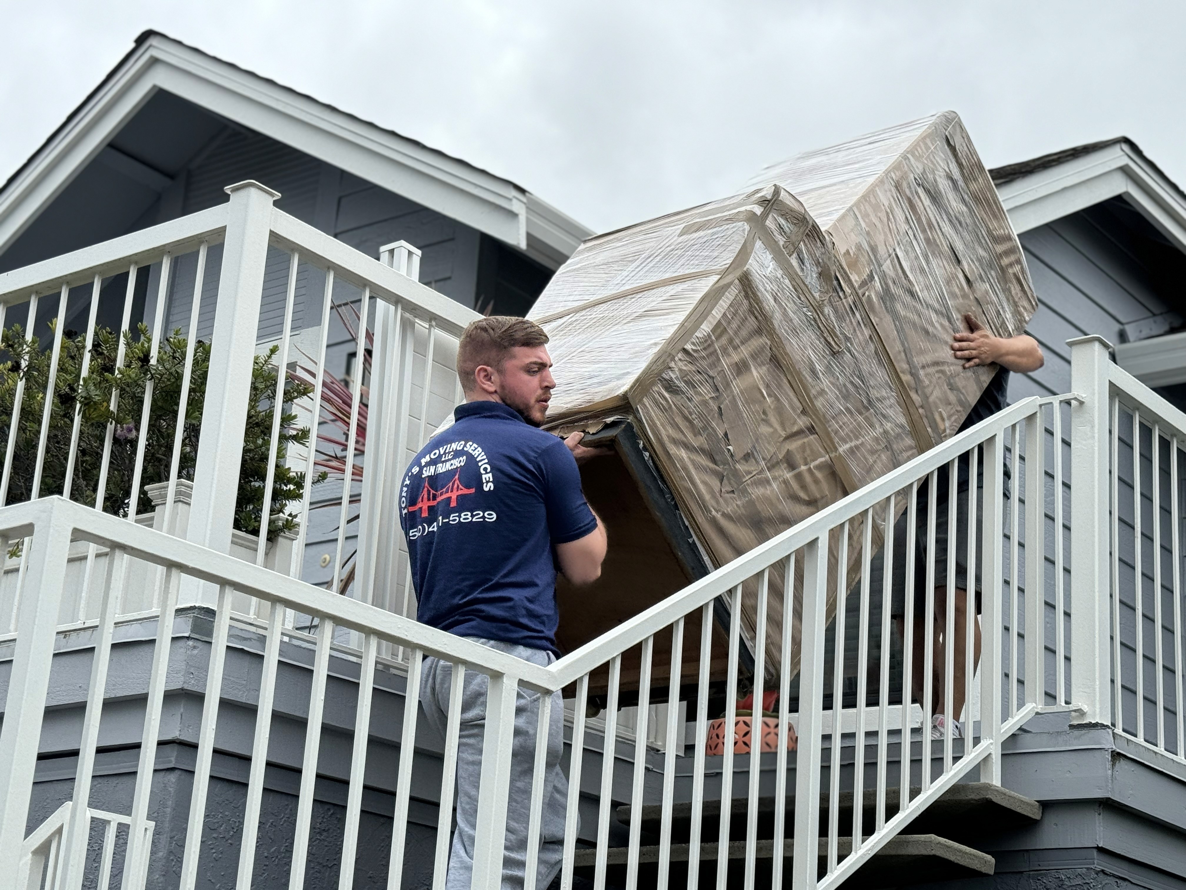 Moving crew carrying a wrapped sofa down exterior stairs