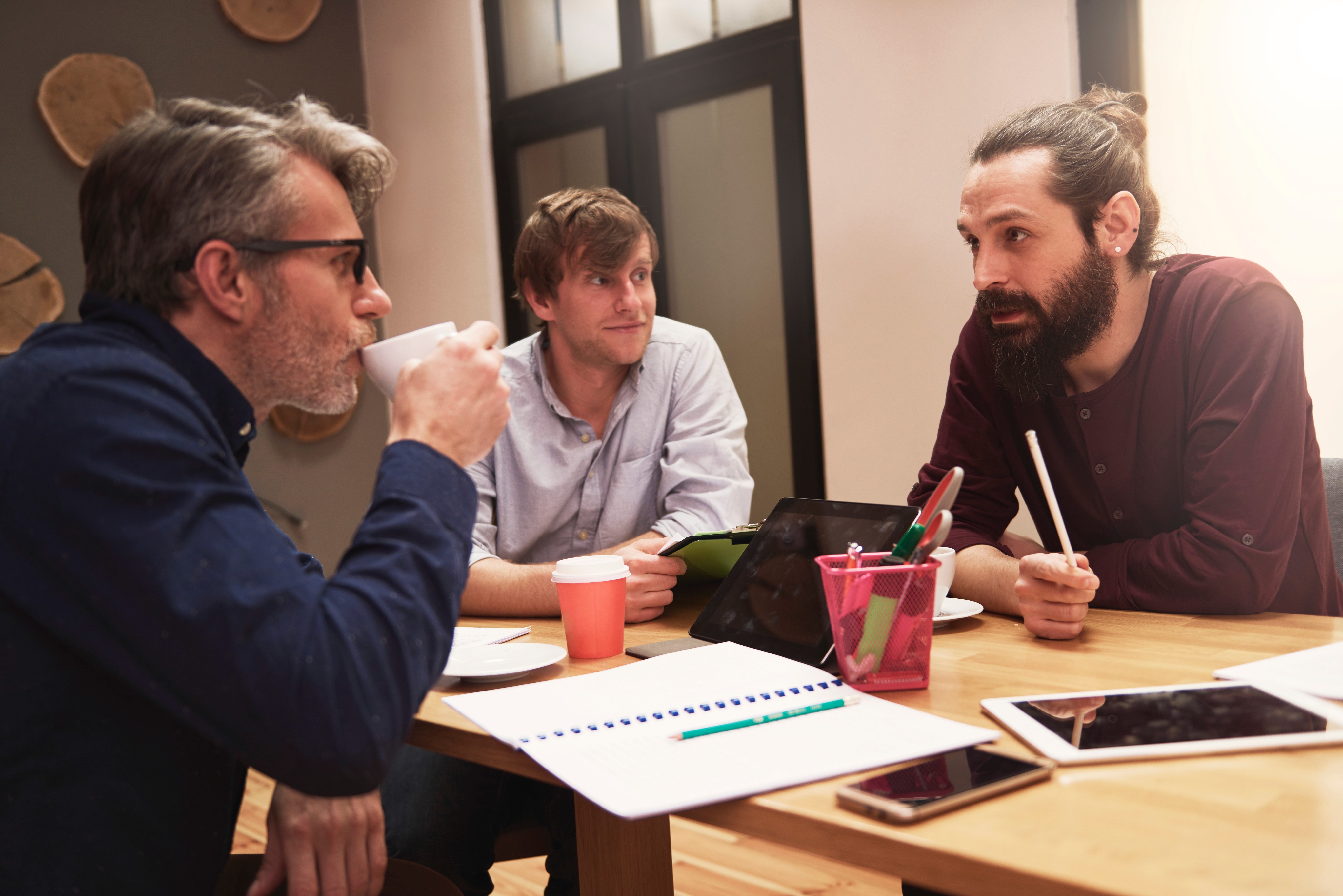 Three men having a discussion at a table with documents and coffee.      Like  Dislike