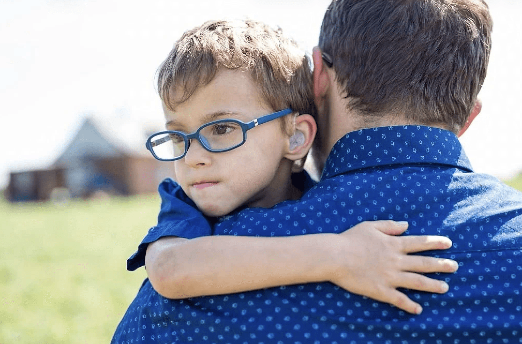 Child with hearing aid hugging man