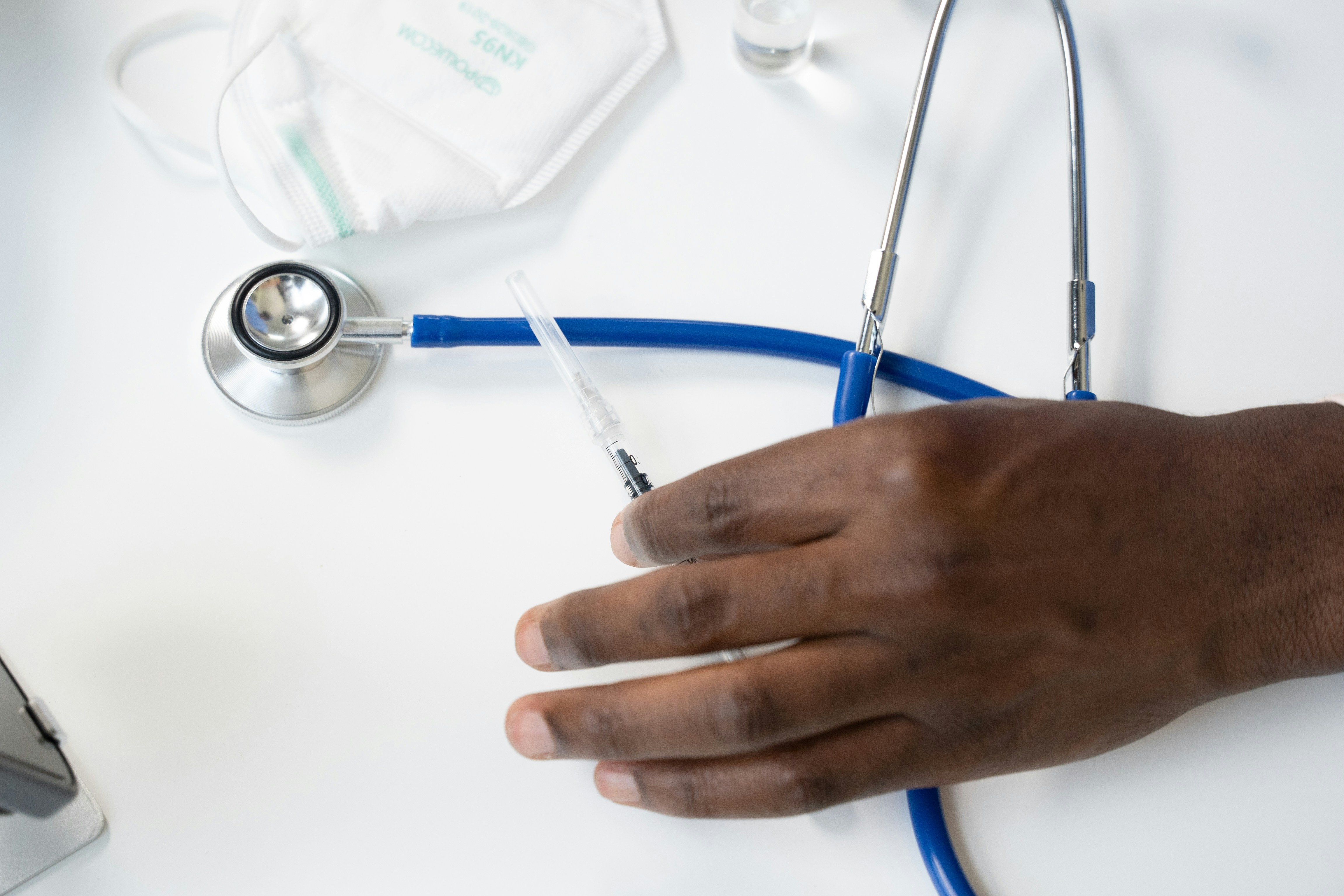 A doctor's hand holding an injection on a table beside a stethoscope