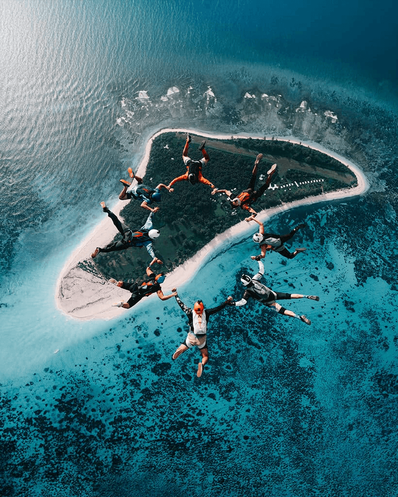 Parachutisten vormen een ring boven een tropisch eiland