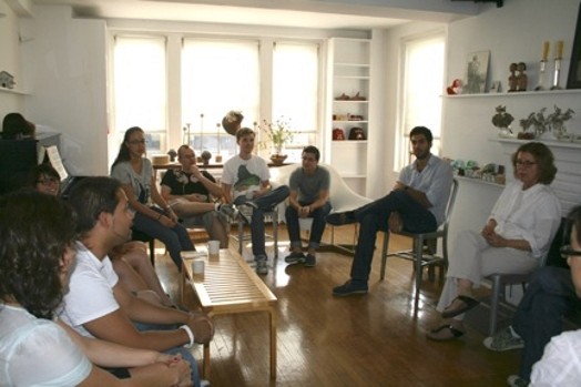 A group of students, siting on chairs in a circle and listening to a lecture given by a woman.