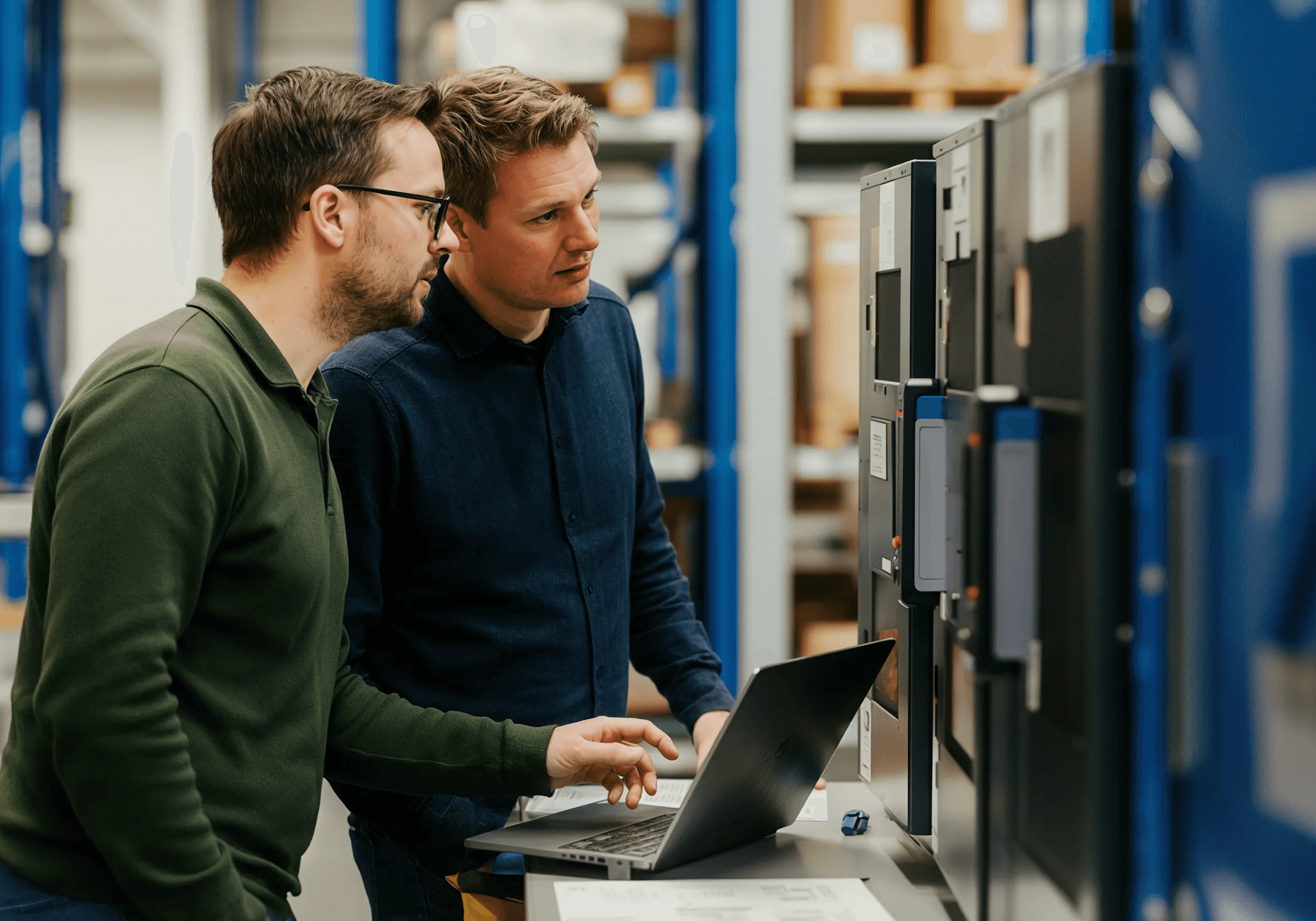 Two engineers reviewing equipment beside a laptop in a workshop
