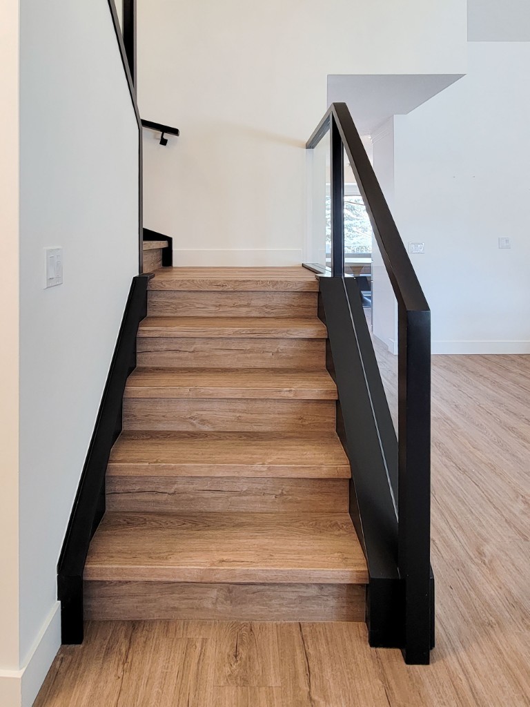 Image of Modern wooden staircase with black metal railing and glass panel in luxury home by KHD Homes.